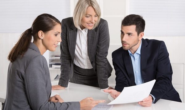 3 personnes en costume se concernant autour d'un document papier